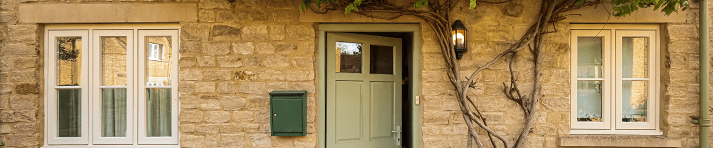 Residential home with a green door, light brown bricks and a large plant growing up the exterior of the home.